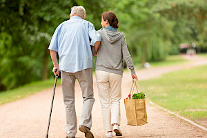Dame trägt älterem Herrn die Tasche mit Einkäufen